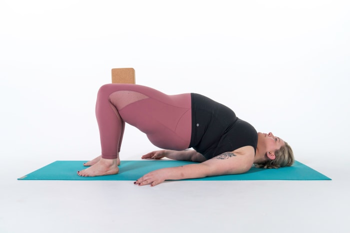 Lie on your back with your knees bent and the soles of your feet planted into the ground. Place a yoga block between your thighs as you press down actively with your heels to help engage both your hamstrings and inner legs. Place your hands next to your hips. Press evenly into your hands and feet to lift your pelvis toward the ceiling. Option: Interlace your hands underneath your back as you draw your shoulder blades closer to your midline. Hold for 5–10 breaths.See also Bridge Pose